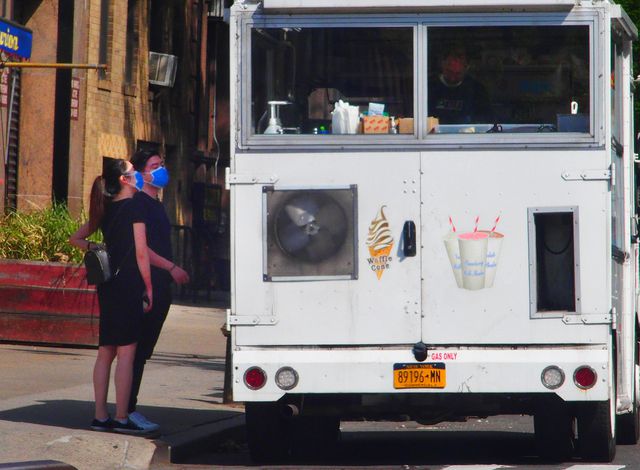 Two people in masks and wearing shorts and t-shirts order ice cream by a Mister Softee truck in Manhattan